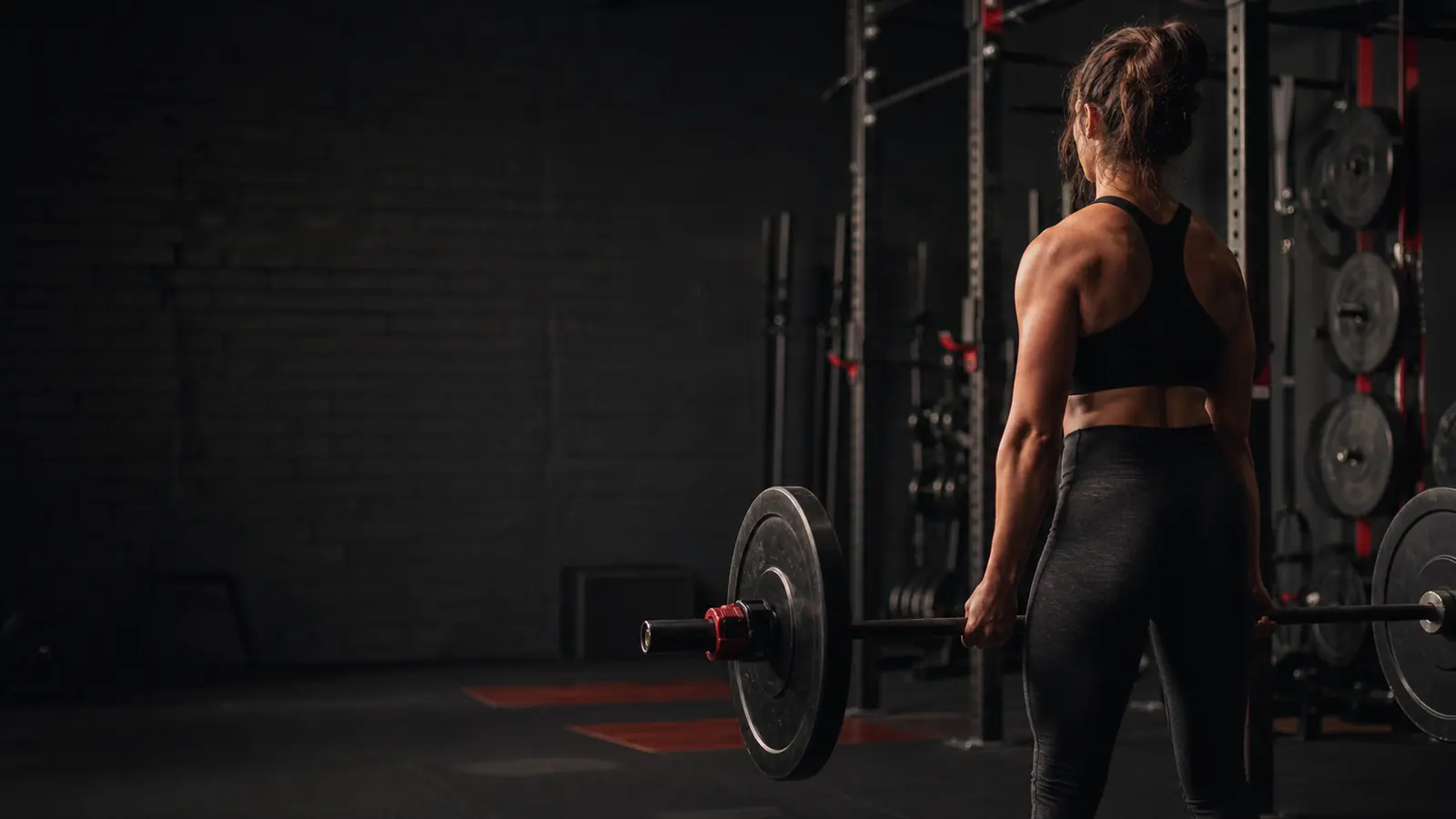 Woman preparing to deadlift in a dark strength gym